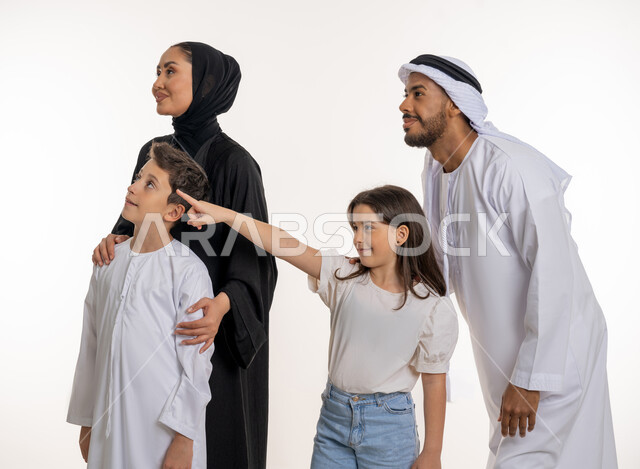 قضاء الأوقات الممتعة برفقة الأبناء, الترابط الأسري والاستمتاع مع العائلة, بورتريه أب وأم عربيان خليجيان إماراتيان مع ولديهما بإيماءات الحب والحنان, مفهوم الأسرة الإماراتية السعيدة, الإشارة إلى شيء ما بعيد والنظر إليه بإيماءات السعادة, خلفية بيضاء
