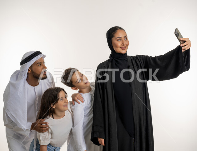 الترابط الأسري والاستمتاع مع العائلة, قضاء الأوقات برفقة الأبناء, بورتريه أب وأم عربيان خليجيان إماراتيان مع ولديهما بإيماءات الحب والحنان, مفهوم الأسرة الإماراتية السعيدة, أخذ صور تذكارية جميلة للعائلة, التقاط صورة سيلفي, خلفية بيضاء