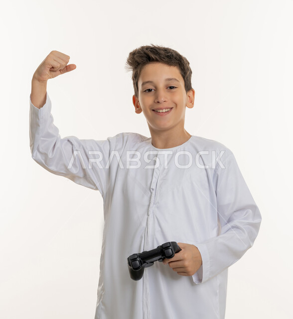 النظر إلى الكاميرا بإيماءات السعادة, رفع اليد بتعبيرات النصر والفوز، بورتريه لفتى عربي خليجي إماراتي يرتدي الكندورة الاماراتيه, اللعب بالبلايستسشن الحديثة، قضاء اوقات ترفيهية ممتعة، خلفية بيضاء