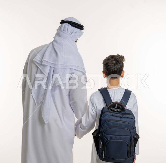 الإمساك بيد الأبناء وتدعيم شعور الأمان, بورتريه من الخلف لطفل عربي خليجي إماراتي يرتدي حقيبة الظهر المدرسية، ارتداء الزي المدرسي، الأب يقوم بإيصال ابنه إلى المدرسة، الاستعداد للفصل الدراسي الجديد، سنة دراسية جديدة، المدارس في الامارات, خلفية بيضاء