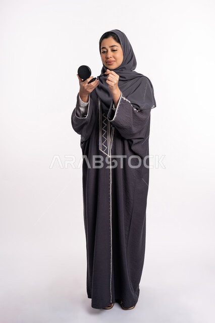 Using eyeliner to highlight the beauty of the eyes, paying attention to beauty and external appearance, educational courses for editorial makeup, a Saudi expert in women’s cosmetics, a close-up portrait of an Arab Gulf-Emirati woman wearing the abaya and hijab, holding a black eyeliner pencil, full body portrait, white background