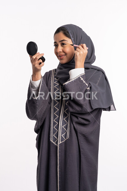 إبراز جمال العينين، مفهوم الإهتمام بالجمال والبشرة والمظهر الخارجي، دورات تعليمية لمكياج تتوريال, خبيرة سعودية لمستحضرات التجميل النسائية، بورتريه مقرب لإمرأة عربية خليجية إماراتية ترتدي العباءة والحجاب تحمل قلم الكحل الأسود، خلفيه بيضاء