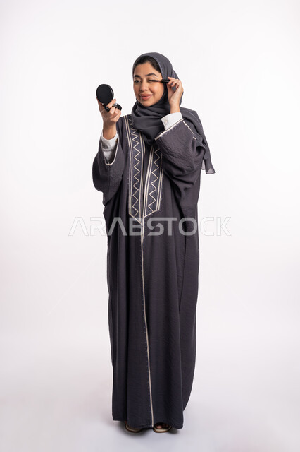 استخدام الايلاينر لإبراز جمال العينين، الإهتمام بالجمال والمظهر الخارجي، دورات تعليمية لمكياج تتوريال, خبيرة سعودية لمستحضرات التجميل النسائية، بورتريه لإمرأة عربية خليجية إماراتية ترتدي العباءة والحجاب تحمل قلم الكحل الأسود، صورة الجسم بالكامل، خلفيه بيضاء