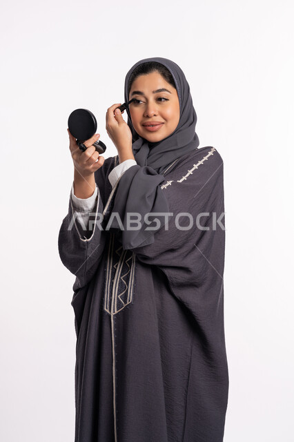 استخدام الماسكرا لإبراز جمال العينين، الإهتمام بالجمال والمظهر الخارجي، دورات تعليمية لمكياج تتوريال, خبيرة سعودية لمستحضرات التجميل النسائية، بورتريه مقرب لإمرأة عربية خليجية إماراتية ترتدي العباءة والحجاب تقوم بوضع الميكاب، خلفيه بيضاء