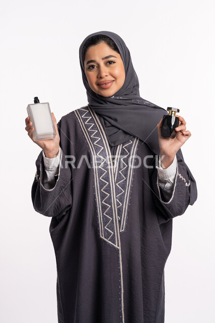 استخدام الزيوت العطرية الطبيعية، التطيب والتعطر بالعود العطري، الحيرة في اختيار الرائحة، منتجات العطور النسائيه، بورتريه لإمرأة عربية خليجية إماراتية ترتدي العباءة والحجاب تقوم برش العطر، الأناقة والإهتمام بالمظهر الخارجي، خلفية بيضاء