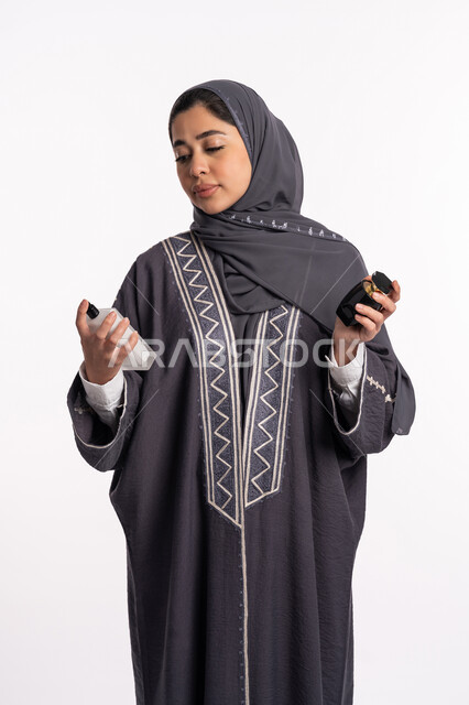 استخدام الزيوت العطرية الطبيعية، التطيب والتعطر بالعود العطري، الحيرة في اختيار الرائحة، منتجات العطور النسائيه، بورتريه لإمرأة عربية خليجية إماراتية ترتدي العباءة والحجاب تقوم برش العطر، الأناقة والإهتمام بالمظهر الخارجي، خلفية بيضاء