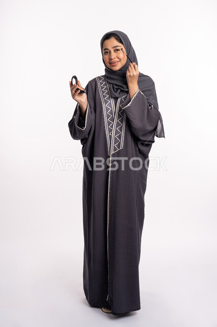 وضع الظلال لإبراز جمال العيون، خبيرة سعودية لمستحضرات التجميل النسائية، بورتريه لإمرأة عربية خليجية إماراتية ترتدي العباءة والحجاب تقوم بوضع الايشادو، دورات تعليمية لمكياج تتوريال، مفهوم الإهتمام بالجمال والبشرة والمظهر الخارجي, صورة الجسم بالكامل، خلفيه بيضاء