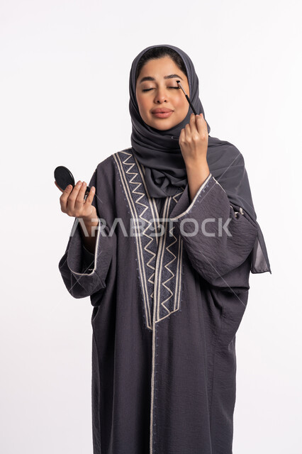 وضع الظلال لإبراز جمال العيون، خبيرة سعودية لمستحضرات التجميل النسائية، بورتريه لإمرأة عربية خليجية إماراتية ترتدي العباءة والحجاب تقوم بوضع الايشادو، دورات تعليمية لمكياج تتوريال، مفهوم الإهتمام بالجمال والبشرة والمظهر الخارجي, خلفيه بيضاء