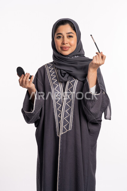 وضع الظلال لإبراز جمال العيون، خبيرة سعودية لمستحضرات التجميل النسائية، بورتريه لإمرأة عربية خليجية إماراتية ترتدي العباءة والحجاب تقوم بوضع الايشادو، دورات تعليمية لمكياج تتوريال، مفهوم الإهتمام بالجمال والبشرة والمظهر الخارجي, خلفيه بيضاء