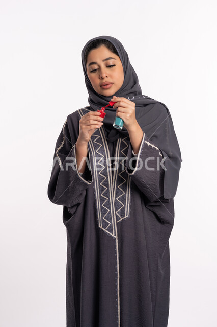 استخدام لون لطلاء الأظافر، خبيرة سعودية لمستحضرات التجميل النسائية، بورتريه لإمرأة عربية خليجية إماراتية ترتدي العباءة والحجاب تحمل بيدها المانيكير، مفهوم الإهتمام بالجمال والمظهر الخارجي، صالون تجميلي نسائي، خلفية بيضاء