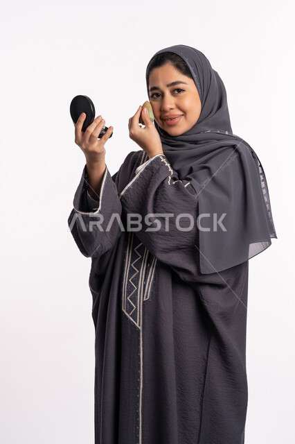 الإهتمام بالجمال والمظهر الخارجي, وضع كريم الأساس لإخفاء عيوب البشرة، دورات تعليمية لمكياج تتوريال، خبيرة سعودية لمستحضرات التجميل، بورتريه لإمرأة عربية خليجية إماراتية ترتدي العباءة والحجاب تحمل بيدها البيوتي بلندر والمرآة، خلفيه بيضاء