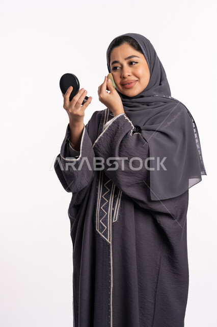 الإهتمام بالجمال والمظهر الخارجي, وضع كريم الأساس لإخفاء عيوب البشرة، دورات تعليمية لمكياج تتوريال، خبيرة سعودية لمستحضرات التجميل، بورتريه لإمرأة عربية خليجية إماراتية ترتدي العباءة والحجاب تحمل بيدها البيوتي بلندر والمرآة، خلفيه بيضاء