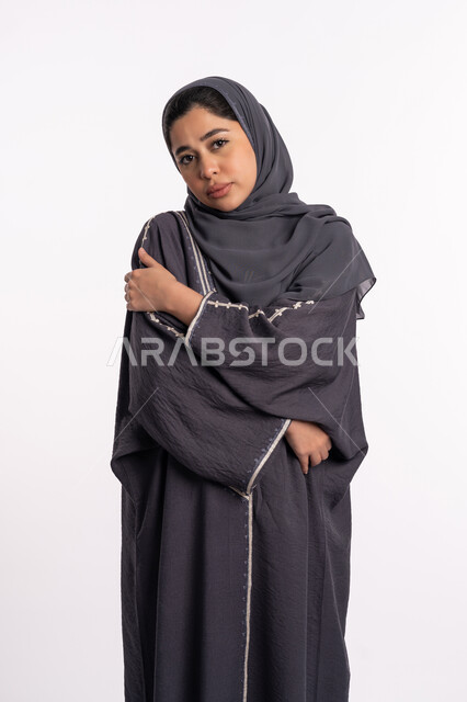 The necessity of early detection of breast cancer, the incidence of the malignant disease, a portrait of an Emirati Gulf Arab woman wearing the hijab and black abaya, looking at the camera with gestures of sadness and depression, a young Saudi woman placing her hand on her shoulder and tilting her head, white background.