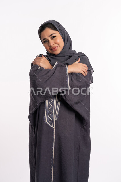The necessity of early detection of breast cancer, the incidence of the malignant disease, a portrait of an Emirati Gulf Arab woman wearing the hijab and black abaya, looking at the camera with gestures of sadness and depression, a young Saudi woman placing her hand on her shoulder and tilting her head, white background.