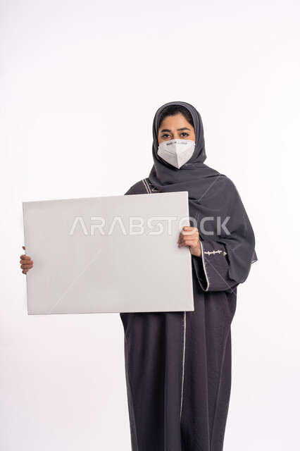 لوحات توعوية لتجنب إنتشار العدوى، الحفاظ على السلامة من كوفيد 19، اتباع الاجراءات الاحترازية للوقاية من فايروس كورونا، بورتريه لإمرأة عربية خليجية إماراتية محجبة ترتدي الكمامة تمسك بيدها موك اب مستطيل أبيض فارغ, خلفية بيضاء