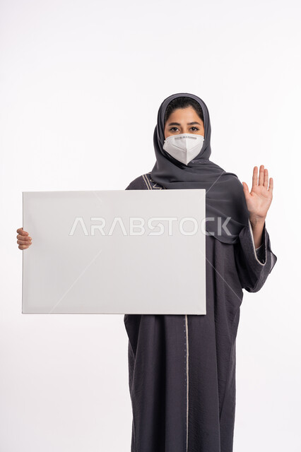 الرفض ومنع الاقتراب، لوحات توعوية لتجنب إنتشار العدوى، اتباع الاجراءات الاحترازية للوقاية من فايروس كورونا، بورتريه لإمرأة عربية خليجية إماراتية محجبة ترتدي الكمامة تمسك بيدها موك اب أبيض فارغ ترفع كف يدها بتعابير التحذير, خلفية بيضاء