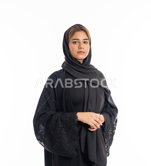 الوقوف باستقامة وثقه بالنفس, الاهتمام بالمظهر الخارجي, شابة سعودية تنظر إلى الكاميرا بايماءات الحزم والجدية، بورتريه مقرب لامرأة عربية خليجية اماراتية محجبة ترتدي عباءة سوداء تقف بأيدي متشبكة، خلفية بيضاء
