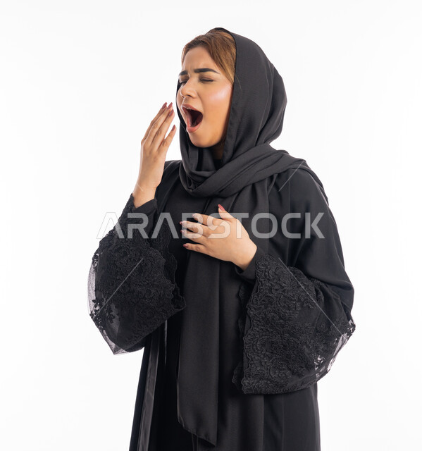 إيماءات النعاس والتعب، شابة سعودية تقوم بالتثاؤب، الحاجة للنوم والراحة،  بورتريه مقرب لامرأة عربية خليجية اماراتية محجبة ترتدي عباءة سوداء تظهر عليها تعابير الكسل و الخمول، السهر لوقت متأخر، خلفية بيضاء