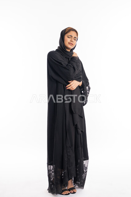 المعاناة من الآلام والأوجاع العصبية والعضلية، التهاب العضلات والمفاصل، الاحساس بالمرض والتعب، بورتريه لامرأة عربيه خليجيه إماراتية ترتدي العباءة السوداء، سيدة سعودية تضع يدها على كتفها بإيماءات تدل على الألم، الجسم بالطول الكامل، خلفية بيضاء