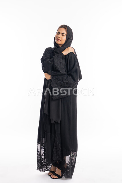 الحاجه للعلاج وطلب المساعده، التهاب العضلات والمفاصل، الإحساس بالمرض والتعب،  بورتريه لامرأة عربيه خليجيه إماراتية ترتدي العباءة السوداء، سيدة سعودية تضع يدها على كتفها بإيماءات تدل على الألم، الجسم بالطول الكامل، خلفية بيضاء