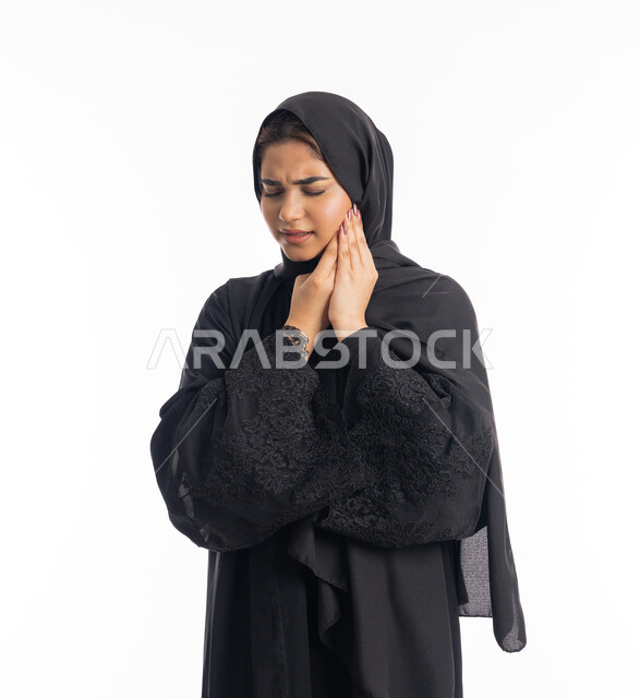 وجع اللثه وتسوس الأضراس، طلب العلاج و المساعده، الحاجه لزيارة الطبيب، سيدة عربية إماراتية ترتدي العباءة السوداء، بورتريه مقرب لامرأه خليجيه سعوديه محجبة تضع يدها على خدها بإيماءات الشعور بألم الأسنان، خلفية بيضاء