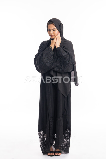 طلب العلاج و المساعده، الحاجه لزيارة الطبيب، سيدة عربية إماراتية ترتدي العباءة السوداء، تسوس الأضراس وإلتهاب اللثه، بورتريه لامرأه خليجيه سعوديه محجبة تضع يدها على خدها بإيماءات الشعور بألم الأسنان، الجسم بالطول الكامل، خلفية بيضاء