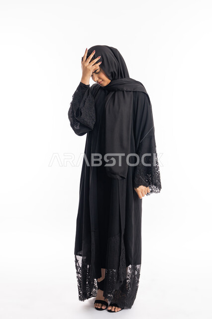 الحاجة للهدوء والراحة، طلب العلاج والمساعده، المعاناة من آلام الشقيقة، الشعور بألم الرأس والصداع، بورتريه لإمرأة خليجية سعودية محجبة تضع يديها على رأسها بايماءات التعب والارهاق، سيدة عربية إماراتية ترتدي العباءة السوداء، الجسم بالطول الكامل، خلفية بيضاء