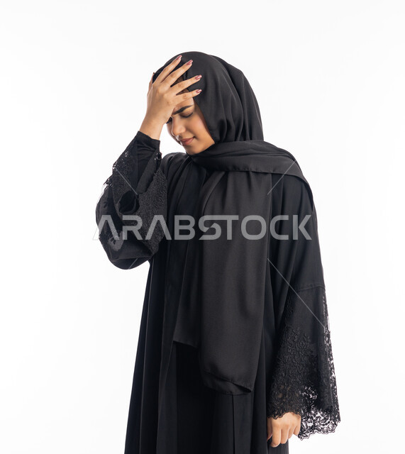 ايماءات التعب والارهاق، الحاجة للهدوء والراحة، طلب العلاج والمساعده، الشعور بألم الرأس والصداع، بورتريه مقرب لإمرأة خليجية سعودية محجبة تضع يديها على رأسها بتعابير المعاناة من آلام الشقيقة، سيدة عربية إماراتية ترتدي العباءة السوداء، خلفية بيضاء
