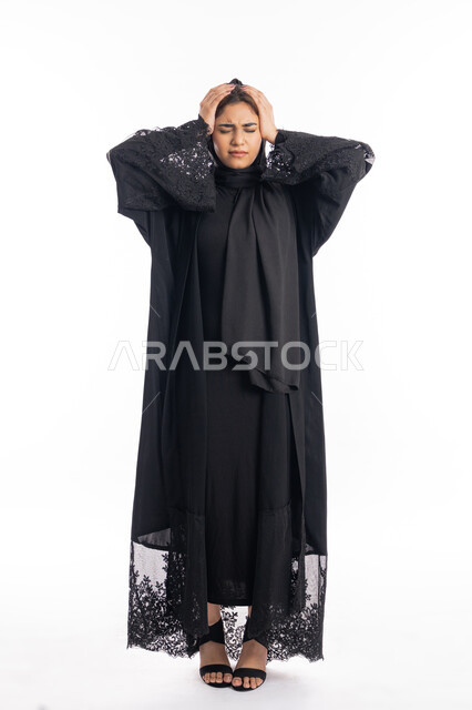 طلب العلاج والمساعده، المعاناة من آلام الشقيقة، الشعور بألم الرأس والصداع، الحاجة للهدوء والراحة، بورتريه لإمرأة خليجية سعودية محجبة تضع يديها على رأسها بايماءات التعب والارهاق، سيدة عربية إماراتية ترتدي العباءة السوداء، الجسم بالطول الكامل، خلفية بيضاء