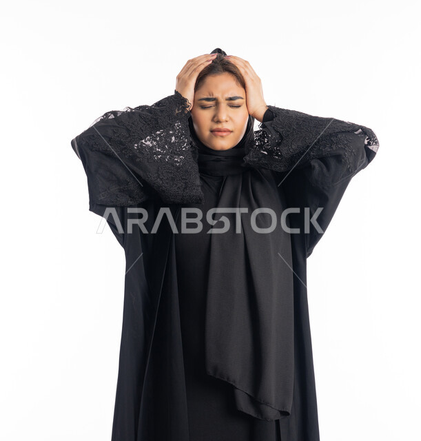 المعاناة من آلام الشقيقة، الشعور بألم الرأس والصداع، طلب العلاج والمساعده، الحاجة للهدوء والراحة، بورتريه مقرب لإمرأة خليجية سعودية محجبة تضع يديها على رأسها بايماءات التعب والارهاق، سيدة عربية إماراتية ترتدي العباءة السوداء، خلفية بيضاء
