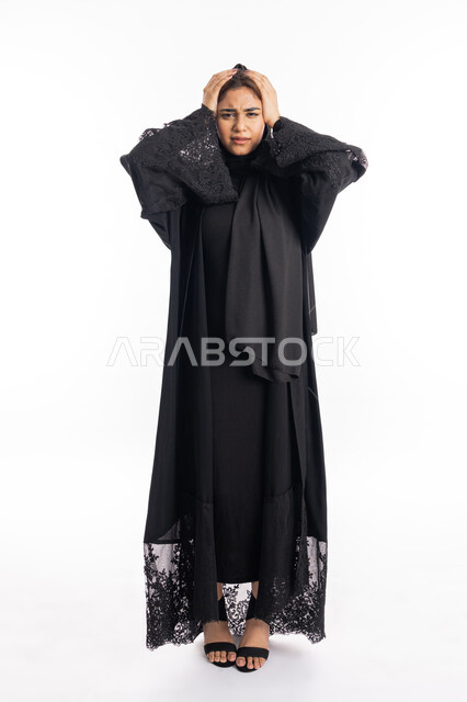 النظر إلى الكاميرا، الاحساس بألم الرأس والصداع، المعاناة من آلام الشقيقة، الحاجة للهدوء والراحة، بورتريه لإمرأة خليجية سعودية محجبة تضع يديها على رأسها بايماءات التعب والارهاق، سيدة عربية إماراتية ترتدي العباءة السوداء، الجسم بالطول الكامل، خلفية بيضاء