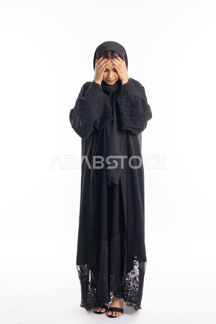 طلب العلاج والمساعده، الاحساس بألم الرأس والصداع، المعاناة من آلام الشقيقة، الحاجة للهدوء والراحة، بورتريه لإمرأة خليجية سعودية محجبة تضع يديها على رأسها بايماءات التعب والارهاق، سيدة عربية إماراتية ترتدي العباءة السوداء، الجسم بالطول الكامل، خلفية بيضاء