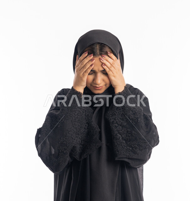 الشعور بألم الرأس والصداع، الحاجة إلى العلاج والمساعده، المعاناة من آلام الشقيقة، الحاجة للهدوء والراحة، بورتريه مقرب لإمرأة خليجية سعودية محجبة تضع يديها على رأسها بايماءات التعب والارهاق، سيدة عربية إماراتية ترتدي العباءة السوداء، خلفية بيضاء