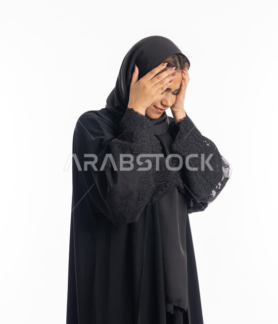 المعاناة من آلام الشقيقة، الشعور بألم الرأس والصداع، الحاجة إلى العلاج والمساعده، الحاجة للهدوء والراحة، بورتريه مقرب لإمرأة خليجية سعودية محجبة تضع يديها على رأسها بايماءات التعب والارهاق، سيدة عربية إماراتية ترتدي العباءة السوداء، خلفية بيضاء