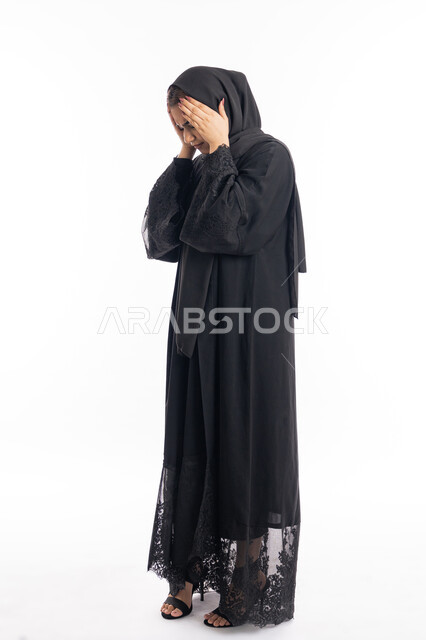 الاحساس بألم الرأس والصداع، الحاجة إلى العلاج والمساعده، المعاناة من آلام الشقيقة، الحاجة للهدوء والراحة، بورتريه لإمرأة خليجية سعودية محجبة تضع يديها على رأسها بايماءات التعب والارهاق، سيدة عربية إماراتية ترتدي العباءة السوداء، الجسم بالطول الكامل، خلفية بيضاء