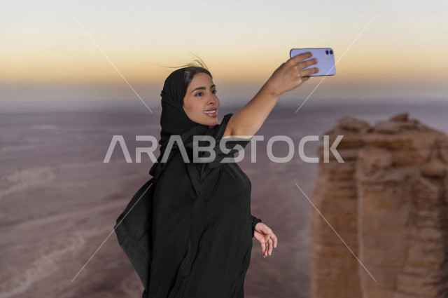 سائحة سعودية خليجية تزور الأماكن السياحية بالمملكة العربية السعودية  ، منطقة مطل نهاية العالم السياحة في الرياض  ، مصورة خليجية تحمل هاتفها المحمول ، تلتقط صور سلفي ، مناطق صحراوية ، جمال الطبيعة السعودية