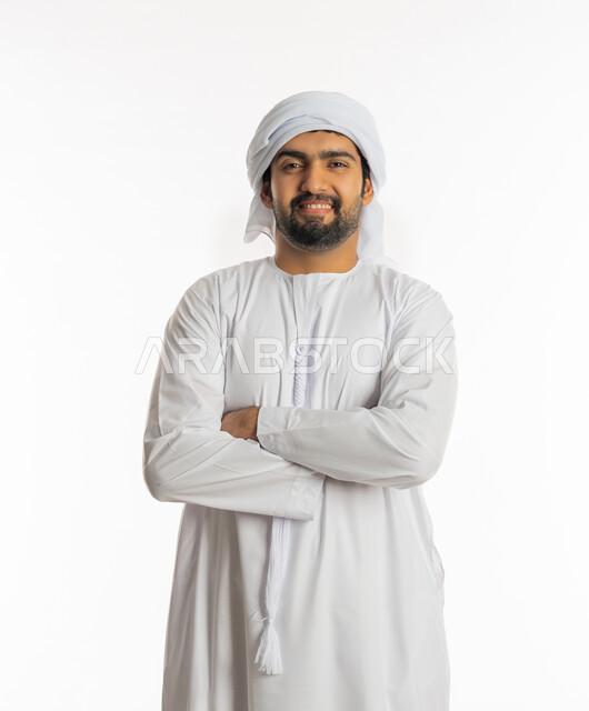 إيماءات الشعور بالسرور و الرضى, الوقوف بإستقامة متكتف اليدين، بورتريه لرجل عربي خليجي إماراتي يرتدي الكندورة و الغترة البيضاء يقف بثقة وينظر الى الكاميرا، خلفية بيضاء