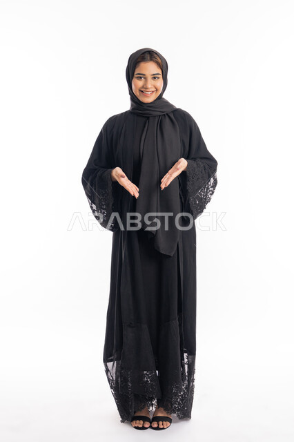 إيماءات الاشارة إلى موقع معين, الاناقة و الاهتمام بالمظهر الخارجي، بورتريه لامراة عربية خليجية اماراتية مبتسمة محجبة ترتدي العباءة السوداء تشير بيديها الى مكان ما، الجسم بالطول الكامل، خلفية بيضاء