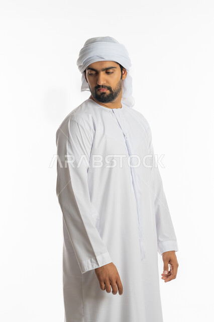 الإهتمام بالمظهر الخارجي، مفهوم الاناقة والرجولة والقوة، بورتريه من الجانب لرجل عربي خليجي اماراتي يرتدي الكندورة الاماراتية والغترة ينظر إلى كتف بايماءات الجدية، تعابير الثقة بالنفس، خلفية بيضاء