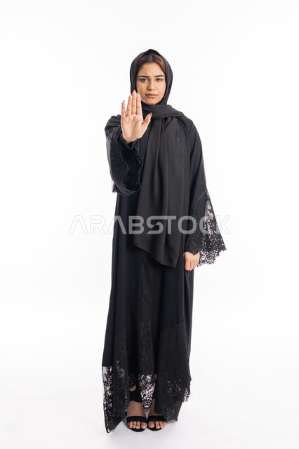 الأمر بالتوقف عن فعل شيء ما، تعابير الرفض والإمتناع، بورتريه لامرأه عربيه خليجيه اماراتية محجة ترتدي عباءة سوداء ترفع يدها بإيماءات تدل على النهي، شابة سعودية انيقة، الشعور بالإنزعاج والغضب، صورة لكامل الجسم، خلفية بيضاء