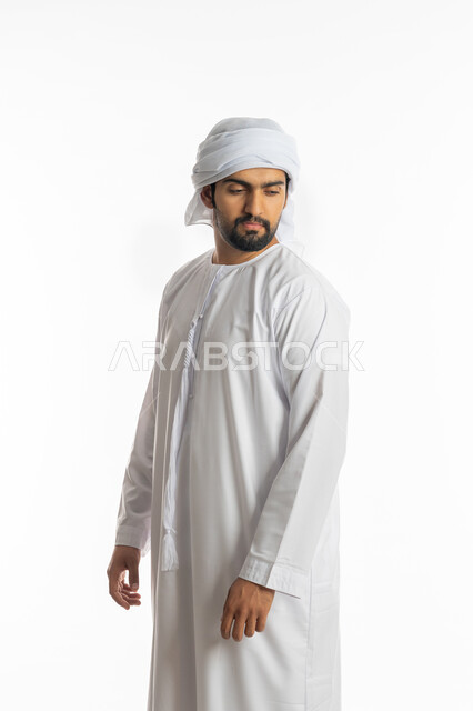 تعابير الثقة بالنفس، الإهتمام بالمظهر الخارجي، مفهوم الاناقة والرجولة والقوة، بورتريه من الجانب لرجل عربي خليجي اماراتي يرتدي الكندورة الاماراتية والغترة ينظر إلى كتف بايماءات الجدية، خلفية بيضاء