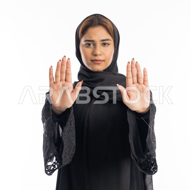 الشعور بالإنزعاج والغضب، تعابير الرفض والإمتناع، الأمر بالتوقف عن فعل شيء ما، بورتريه مقرب لامرأه عربيه خليجيه اماراتية محجة ترتدي عباءة سوداء ترفع يديها بإيماءات تدل على النهي، شابة سعودية انيقة، خلفية بيضاء
