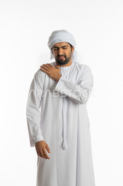الحاجة للعلاج والاستشارة الطبية، تعابير الألم و وجع الظهر، الشعور بالمرض والإرهاق، بورتريه لرجل عربي خليجي اماراتي يرتدي الكندورة الاماراتية والكندورة يضع يده على كتفه بايماءات التعب، خلفية بيضاء