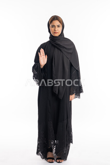 الأمر بالتوقف عن فعل شيء ما، تعابير الرفض والإمتناع، بورتريه لامرأه عربيه خليجيه اماراتية محجة ترتدي عباءة سوداء ترفع يدها بإيماءات تدل على النهي، شابة سعودية انيقة، الشعور بالإنزعاج والغضب، صورة لكامل الجسم، خلفية بيضاء