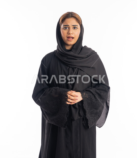 الانزعاج لسماع الأخبار السيئة، الشعور بالحزن والضجر، بورتريه لإمرأة عربية خليجية اماراتية محجبة ترتدي عباءة سوداء تقف بايدي متشابكة، شابة سعودية تنظر إلى الكاميرا بايماءات الصدمة، خلفية بيضاء