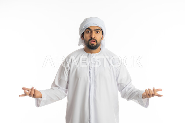 Interrogative on a specific topic, a portrait close to an Emirati Gulf Arab man who wears the Emirati kandora and the white turban, raises his hands up with gestures of lack of knowledge, wondering and inquiring about something, mystery and lack of clarity, white background