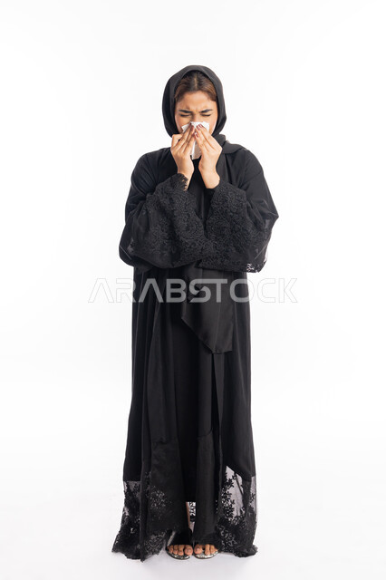 الشعور بالتعب والمرض، الإصابة بفايروس كورونا كوفيد19، استعمال المناديل الورقيه أثناء العطس، بورتريه لامرأه عربيه خليجيه اماراتية محجبة ترتدي عباءة سوداء، شابة سعودية انيقة، إيماءات وجه ويدين تدل على العطاس، صورة لكامل الجسم، خلفية بيضاء