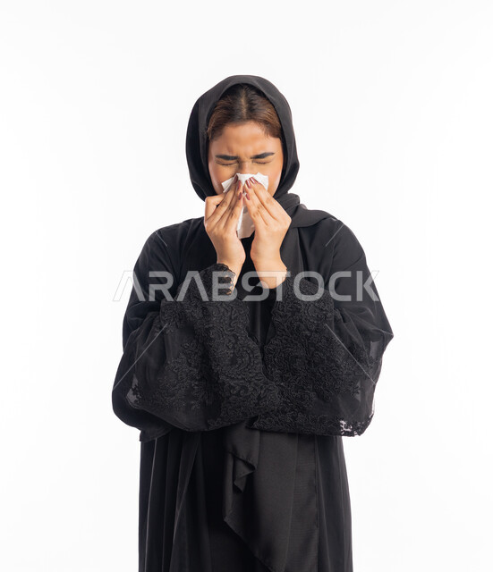 إيماءات وجه ويدين تدل على العطاس، شابة سعودية انيقة، استعمال المناديل الورقيه أثناء العطس، الإصابة بفايروس كورونا كوفيد19، الشعور بالتعب والمرض، بورتريه لامرأه عربيه خليجيه اماراتية محجبة ترتدي عباءة سوداء، خلفية بيضاء