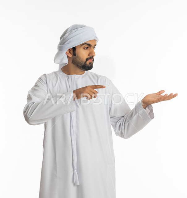 إيماءات حمل ورفع شيء ما، بورتريه لرجل عربي خليجي إماراتي يرتدي الكندورة الإماراتية والعمامة البيضاء يشير باصبع السبابة ليده، الإشارة نحو هدف ما، حركة أصابع وإشارات، خلفية بيضاء
