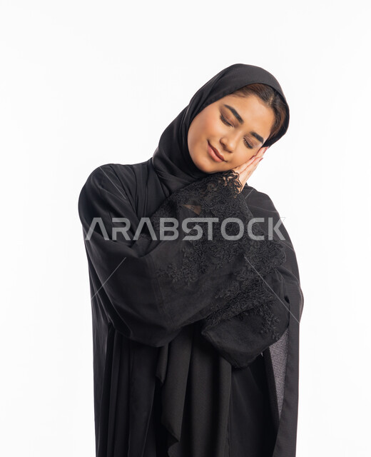 تعابير الكسل والخمول، الحاجة للنوم والراحة، شابة سعودية انيقة، بورتريه لإمرأه عربية خليجية اماراتية محجبة ترتدي عباءة سوداء تضع يديها تحت رأسها بإيماءات تدل على النعاس والتعب، السهر لوقت متأخر، خلفية بيضاء